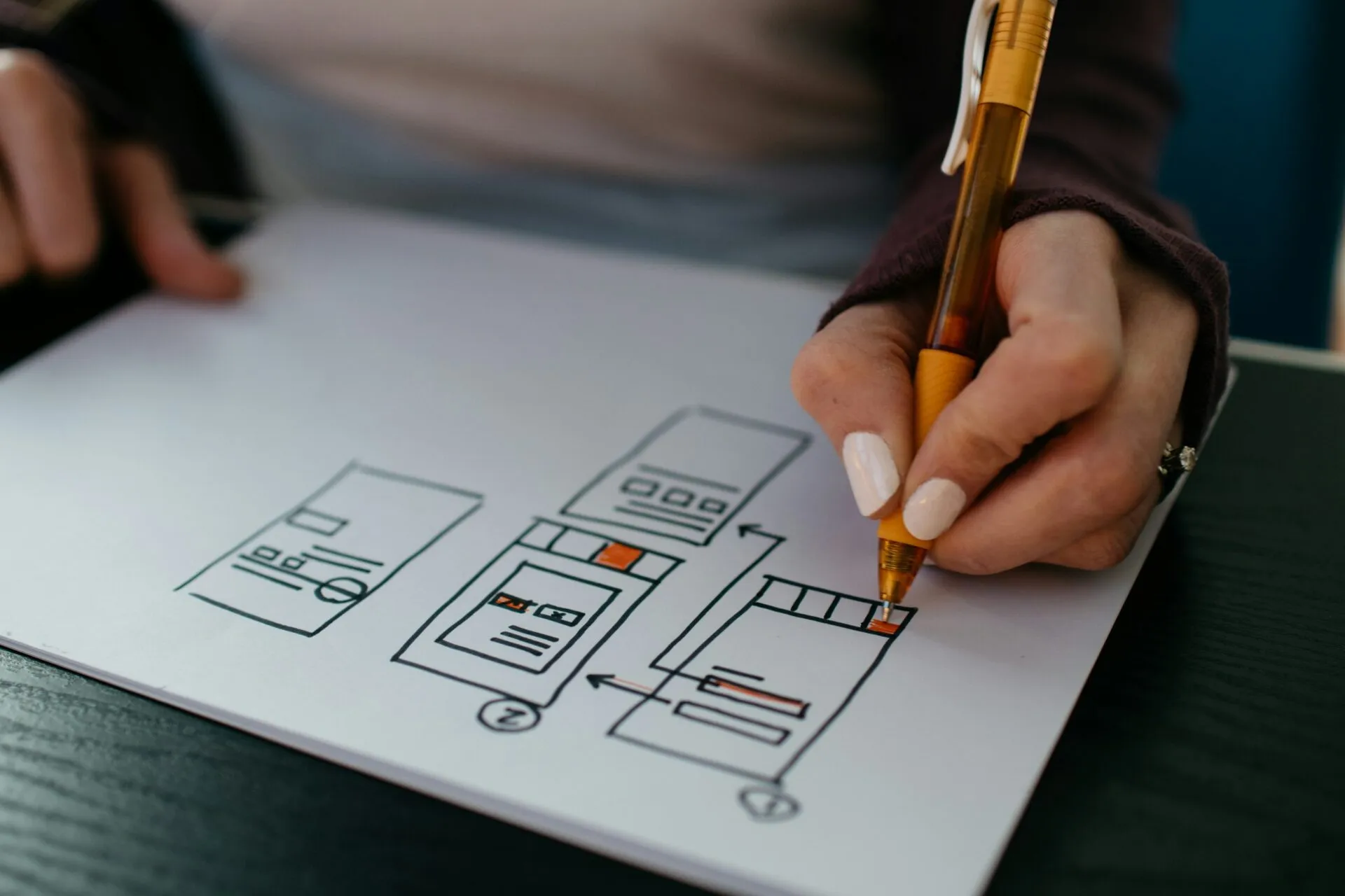 Hand sketching mobile wireframes on paper with an orange pen