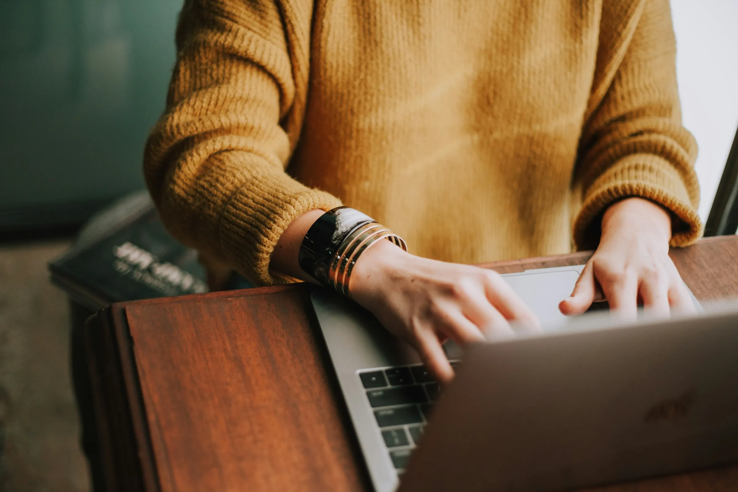Person typing on a laptop at a wooden desk, the setup of a solo freelance designer