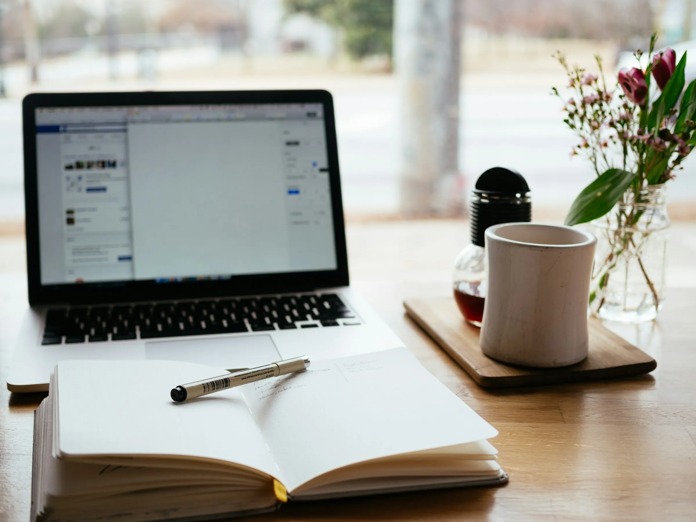 Open notebook and pen in front of a laptop on a wooden table