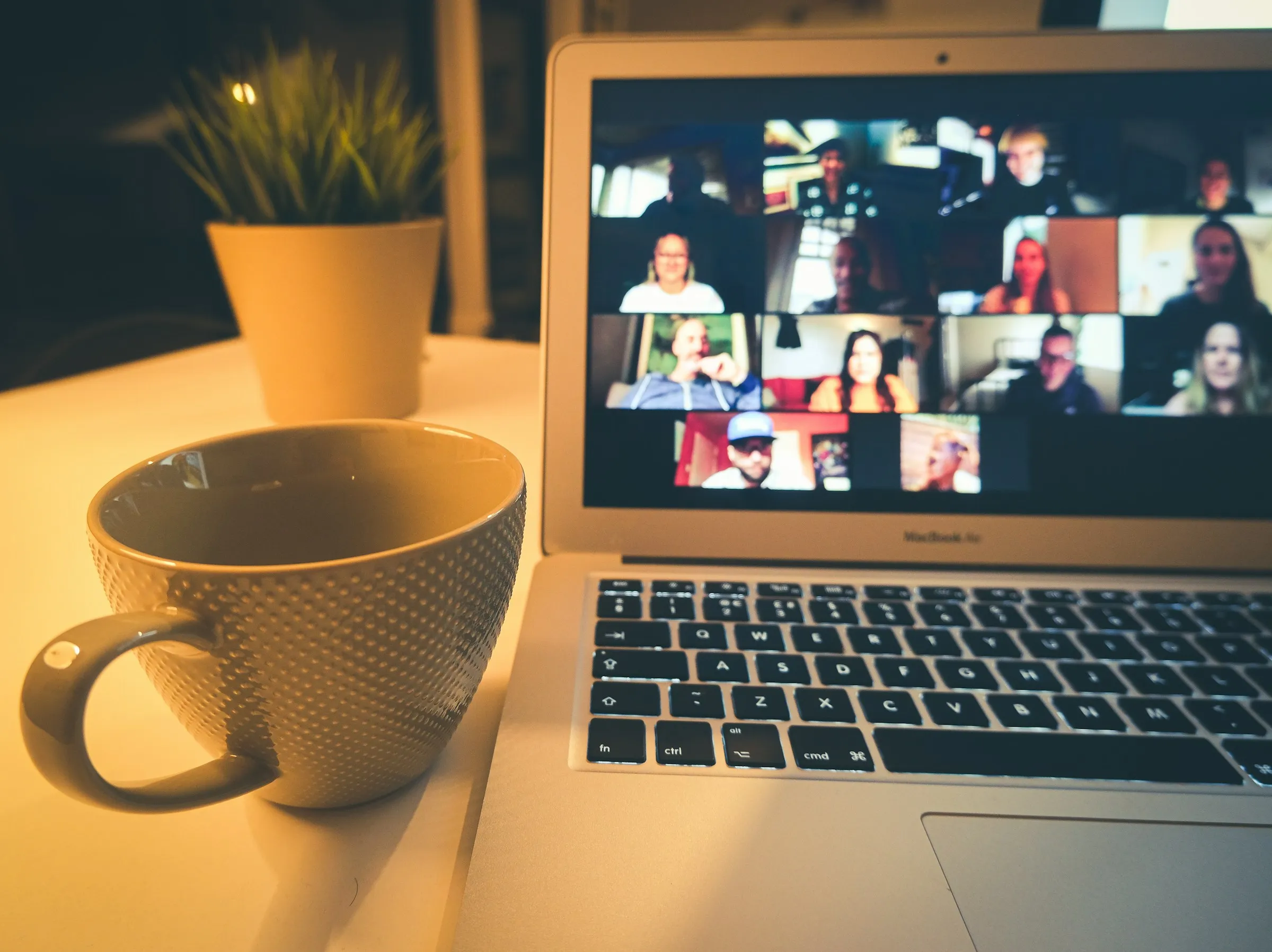 Laptop on a desk showing a video call grid next to a coffee cup