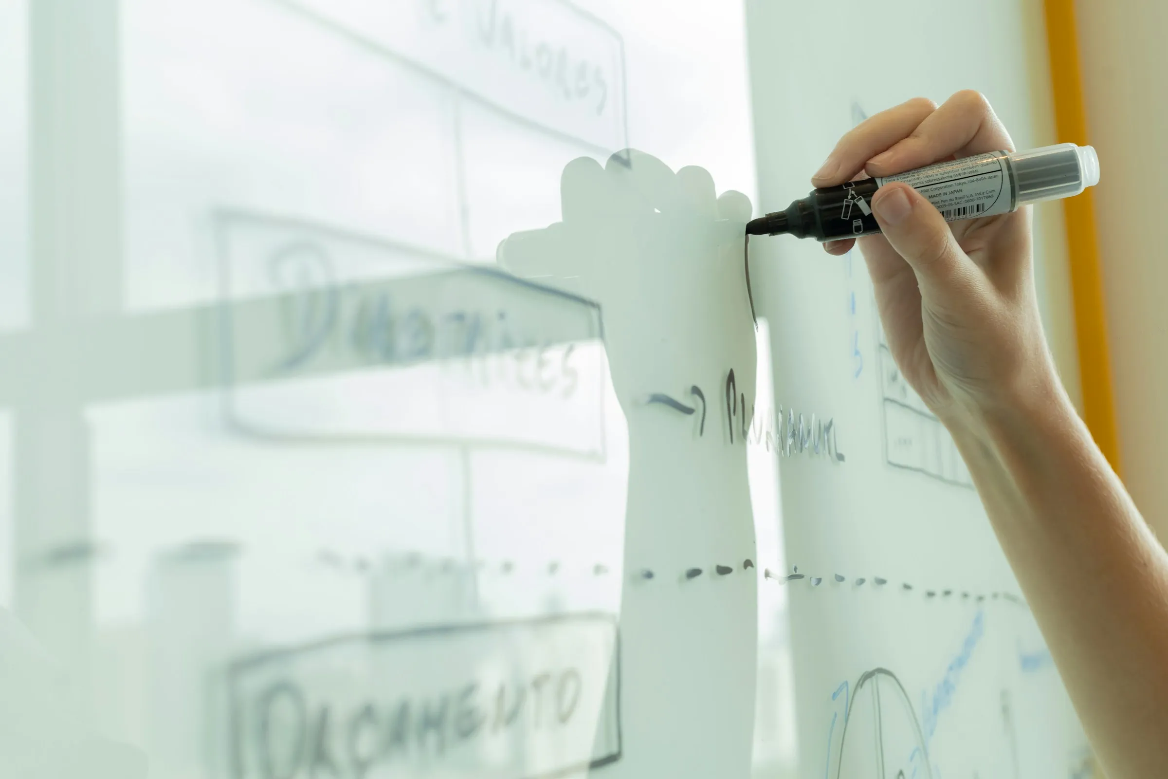A hand sketching a product diagram with a black marker on a glass whiteboard