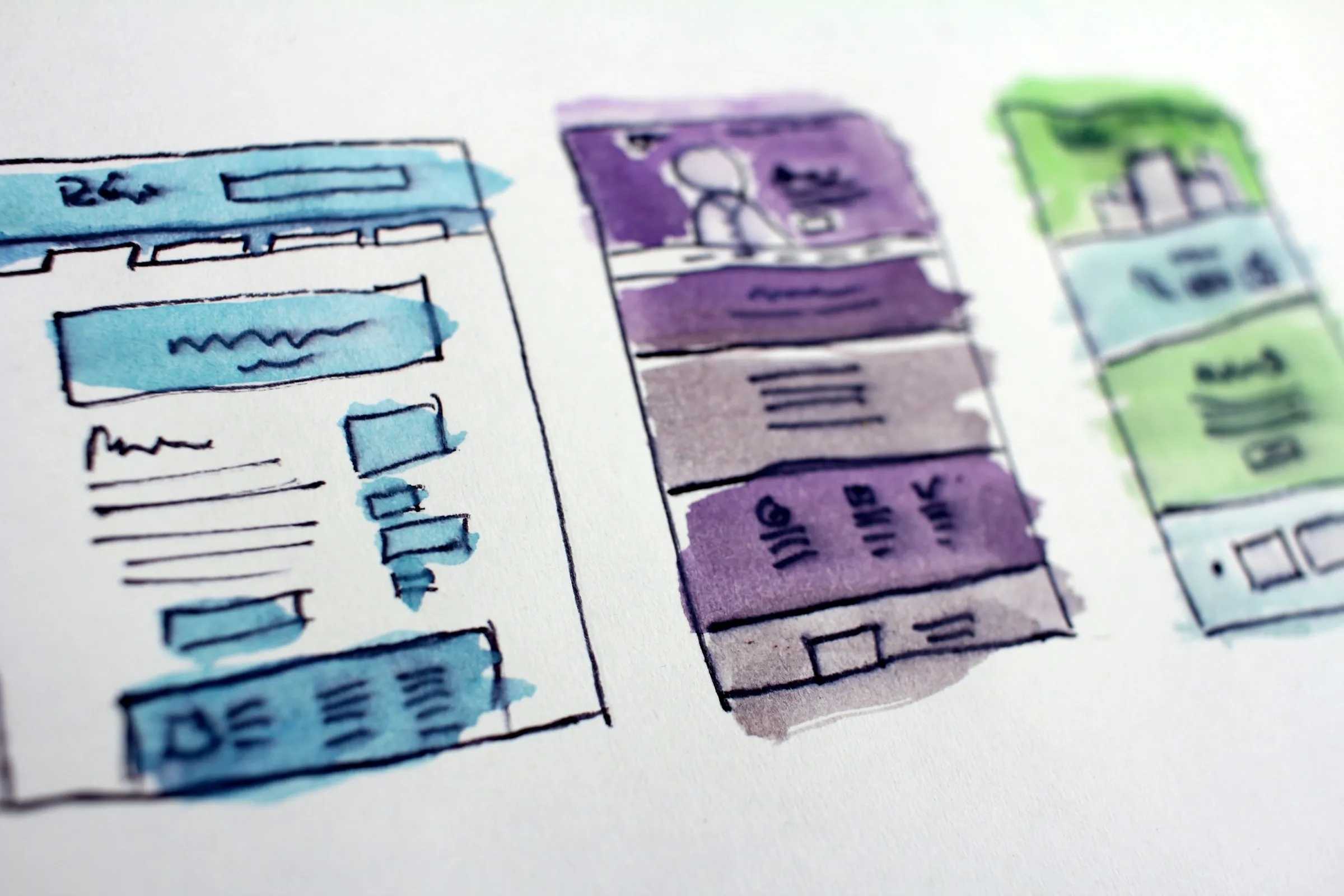 Watercolor wireframe sketches of three website page layouts on white paper